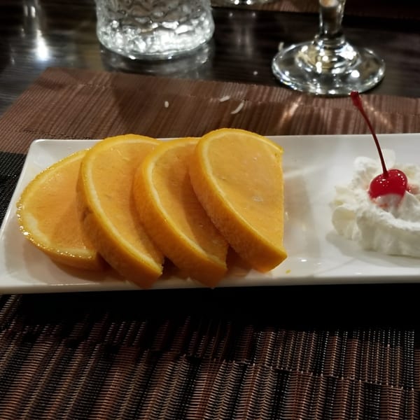 Four orange slices and a dollop of whipped cream with a cherry on a white plate.