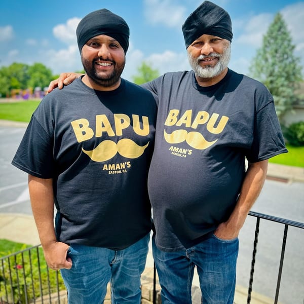 Two smiling Indian men, possibly father and son, wearing matching "Bapu Aman's Easton, PA" t-shirts.