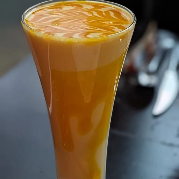 Aman's Artisan Indian Cuisine's mango lassi in a tall glass with decorative swirls on top.