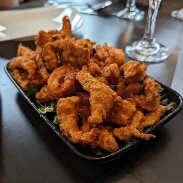 A black rectangular plate filled with golden-brown fried Indian pakora, garnished with green lettuce.