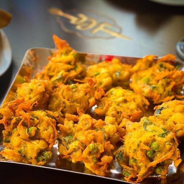 A close-up of golden-fried Indian pakoras with green peas on a silver tray.