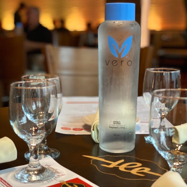 A Vero water bottle and empty wine glasses on a dark table at Aman's Artisan Indian Cuisine.