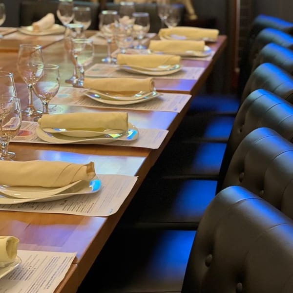 Long dining table set with plates, rolled napkins, and wine glasses, with dark chairs.