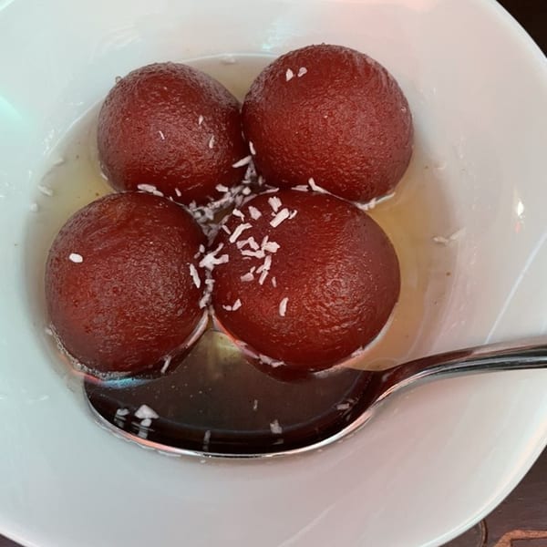 Four gulab jamun, Indian fried dough balls in syrup, topped with shredded coconut in a white bowl.