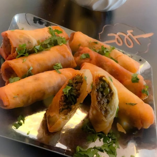 Crispy Indian spring rolls, one cut open to show a savory meat and pea filling, garnished with cilantro.