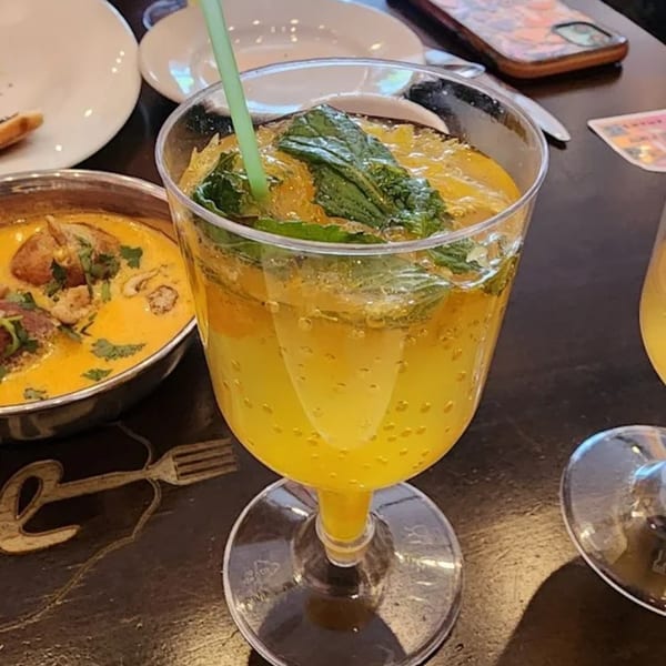 Aman's Artisan Indian Cuisine's vibrant yellow drink with mint and a green straw, next to a bowl of curry.