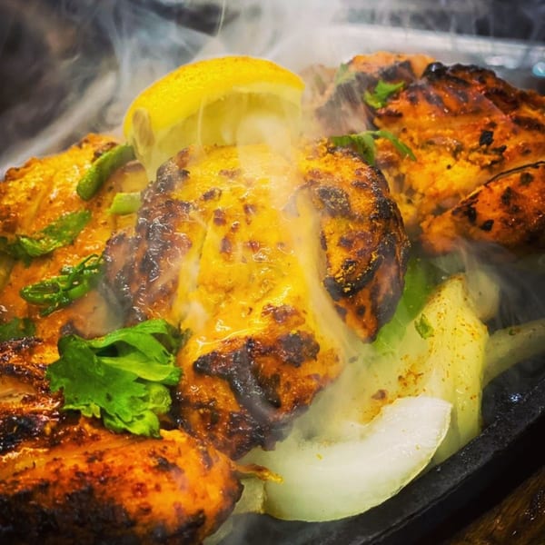 Sizzling Indian chicken tikka with onions, green peppers, cilantro, and a lemon wedge.