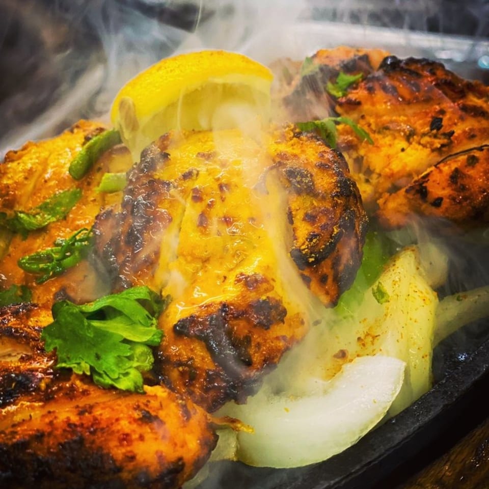 Sizzling Indian chicken tikka with onions, green peppers, cilantro, and a lemon wedge.