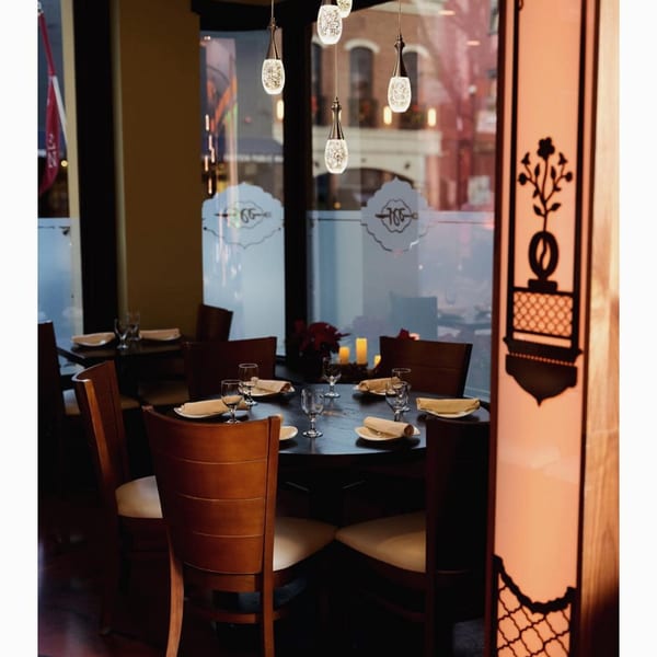 Aman's Artisan Indian Cuisine dining room with set tables, modern pendant lights, and decorative window decals.
