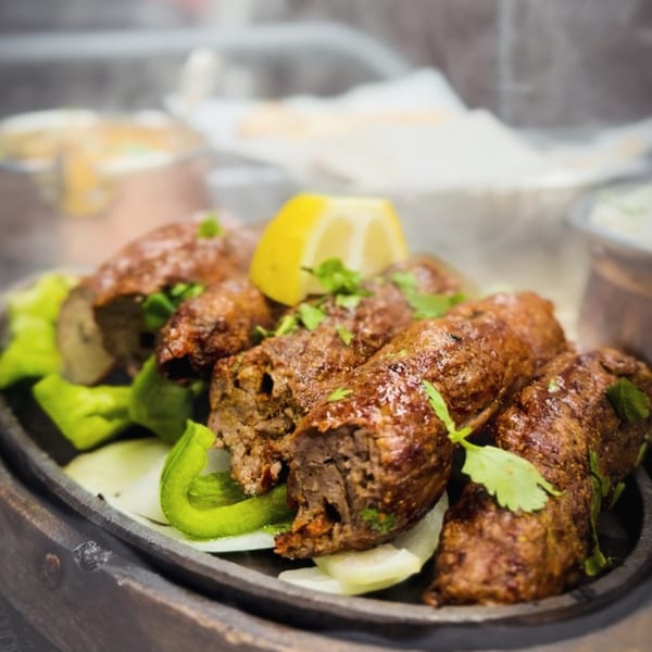Indian seekh kebabs, garnished with cilantro and a lemon wedge, served on a dark platter.