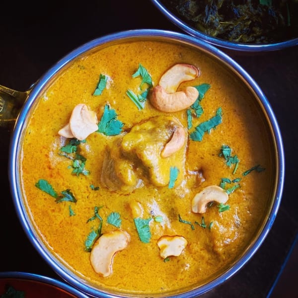 Aman's Artisan Indian Cuisine's creamy chicken curry with cashews and cilantro in a metal bowl.