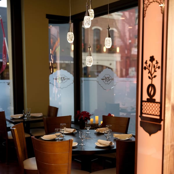 Interior of Aman's Artisan Indian Cuisine, featuring a set table, decorative lighting, and window views.