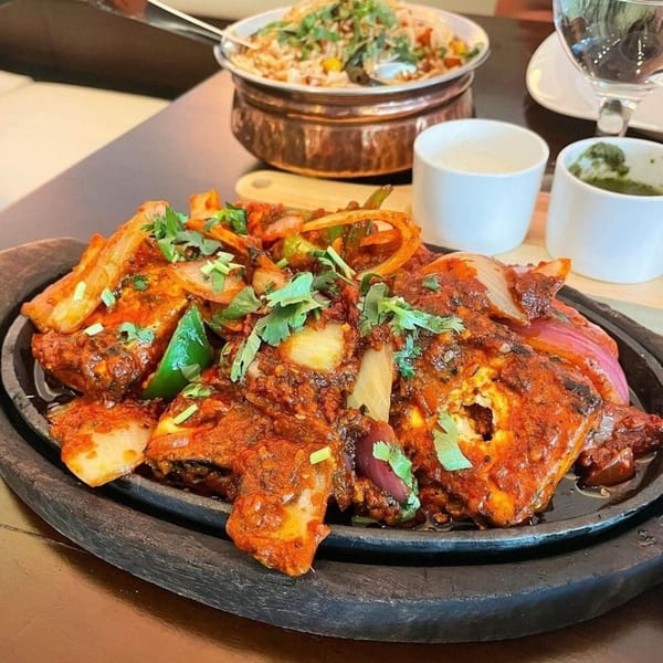 Aman's Artisan Indian Cuisine's sizzling paneer tikka with onions, peppers, and cilantro, served with rice and sauces.